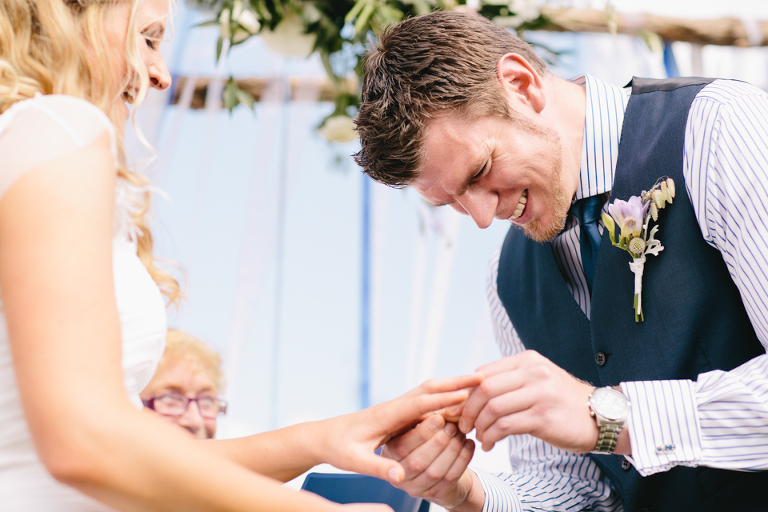 Groom putting ring on finger and laughing at ceremony
