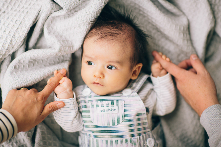  newborn baby in blanket holding onto hands Wellington in home family photography natural light