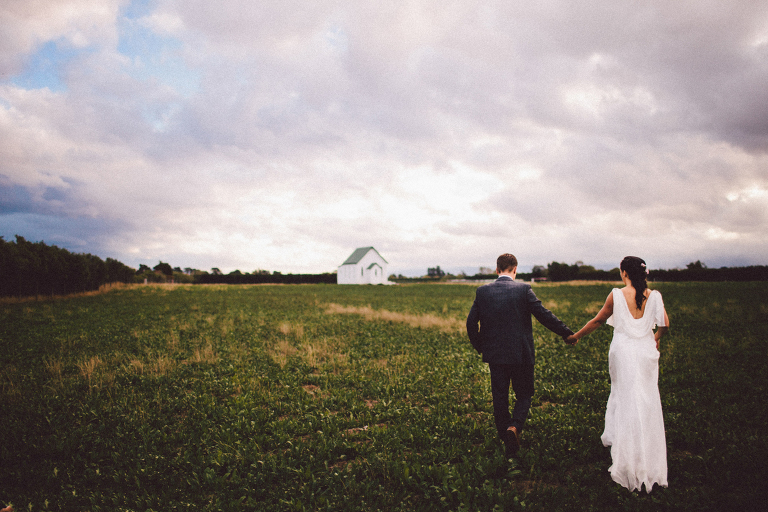 bride and groom holding hands in a rustic field chapel in the background Burnside Church Martinborough Wedding natural light 