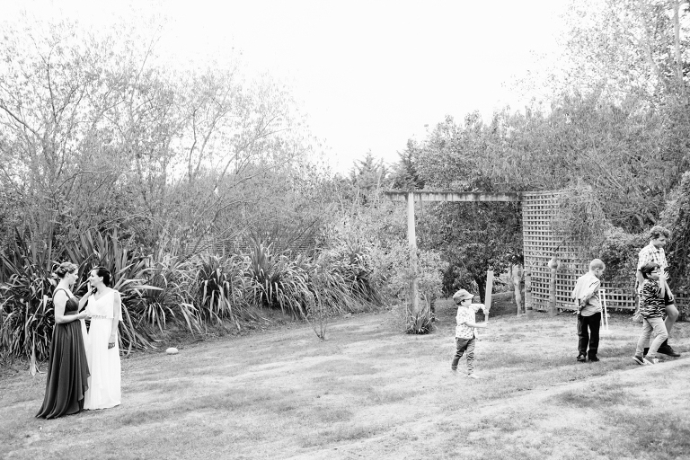 bride talking to bridesmaid with children playing Burnside Church Martinborough Wedding natural light black and white