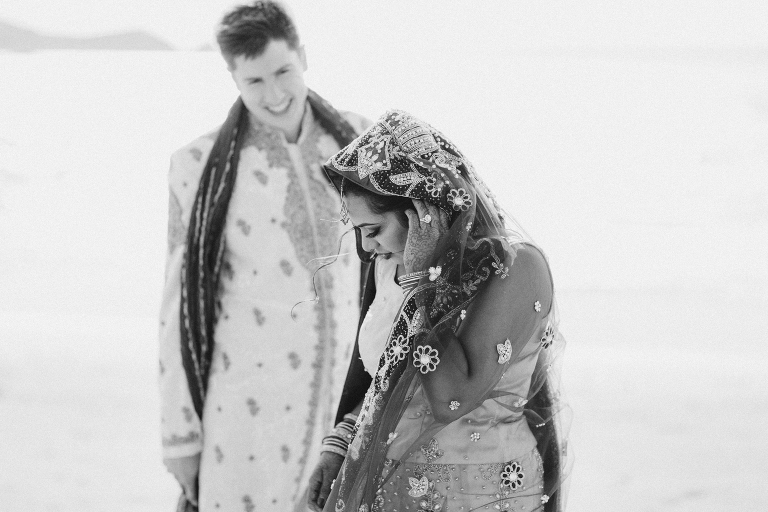 groom smiling at bride walking by water on beach Pauatahanui Inlet Wellington wedding natural light black and white