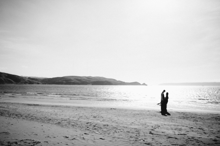 bride and groom standing in background by ocean Pauatahanui Inlet Wellington wedding natural light black and white