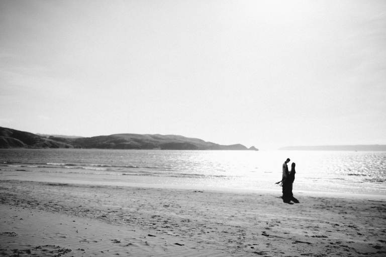 bride and groom standing in background by ocean Pauatahanui Inlet Wellington wedding natural light black and white