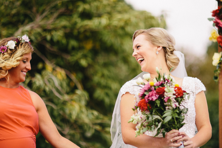 bride laughing at bridesmaid with bouquet during ceremony Martinborough Brackenridge Estate wedding natural light 