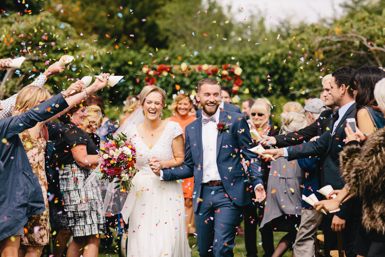 Bride and groom walking down aisle with flowers thrown at them after ceremony Martinborough Brackenridge Estate wedding natural light 