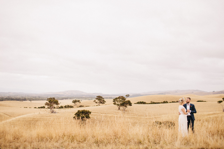 bride and groom in foreground in rustic field Martinborough Brackenridge Estate wedding natural light 