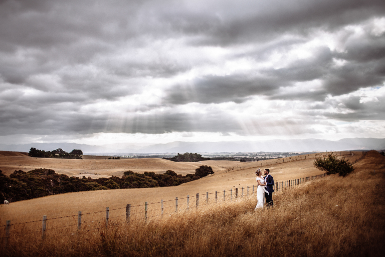 bride and groom in rustic field under cloudy skies Martinborough Brackenridge Estate wedding natural light 
