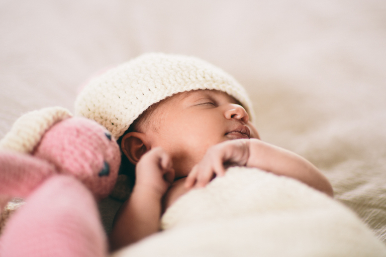 baby girl on bed wrapped in blanket with hat on asleep next to a pink stuffed bear Newborn Photography Wellington natural light