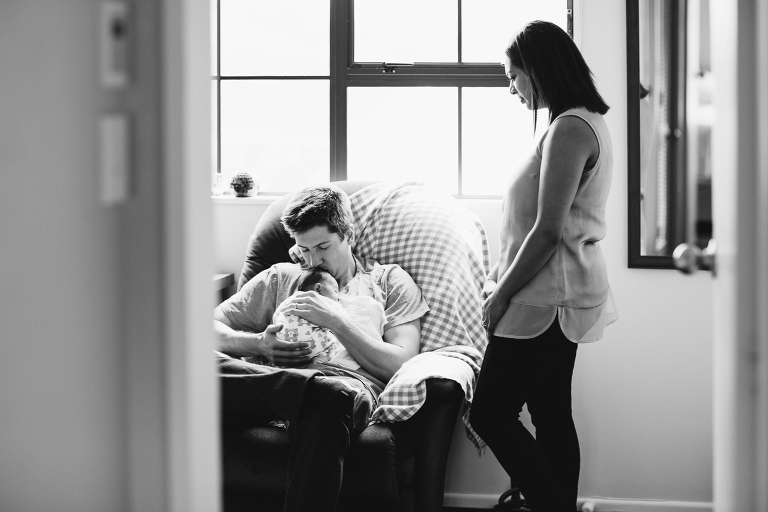 father holding baby girl on his chest with mom looking on Newborn Photography Wellington black and white