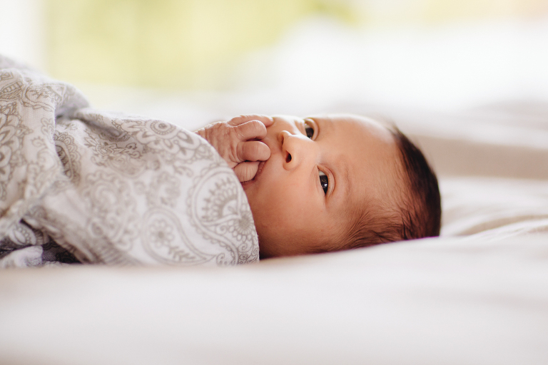 baby girl on bed wrapped in blanket with hand in mouth Newborn Photography Wellington natural light