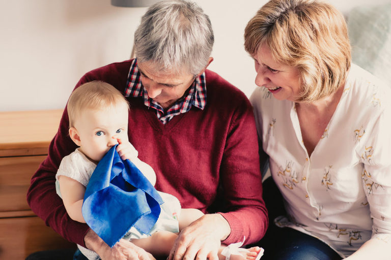 grandmother and granfather with baby girl looking down at her smiling natural light In-Home Photography First Birthday Party