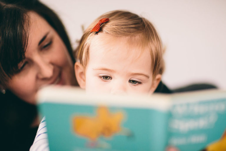 baby sitting in woman's lap reading a book natural light In-Home Photography First Birthday Party