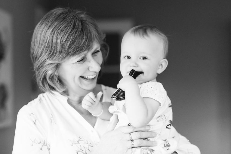 baby girl being held by grandmother while holding a toy black and white natural light In-Home Photography First Birthday Party