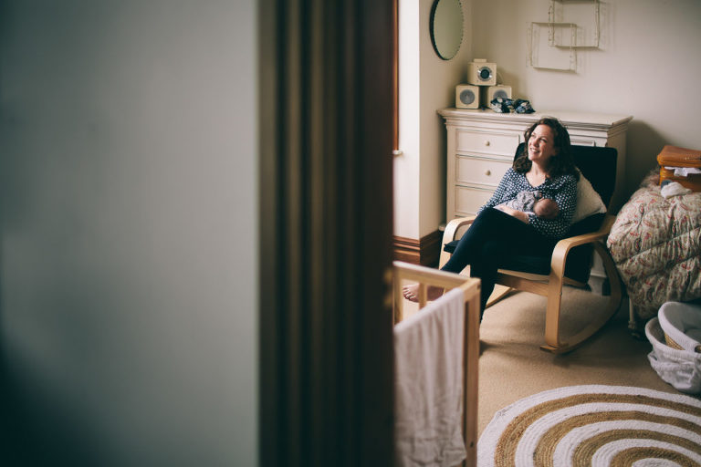 brunette mum sitting with newborn baby girl in rocking chair in nursery newborn photography in-home Wellington natural light 