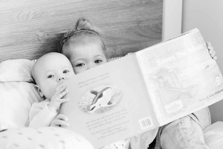 sisters cudding on bed reading book natural light black and white Family photos in-home Wellington