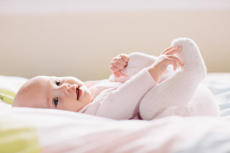 baby girl on bed smiling playing with feet natural light Wellington Family photography