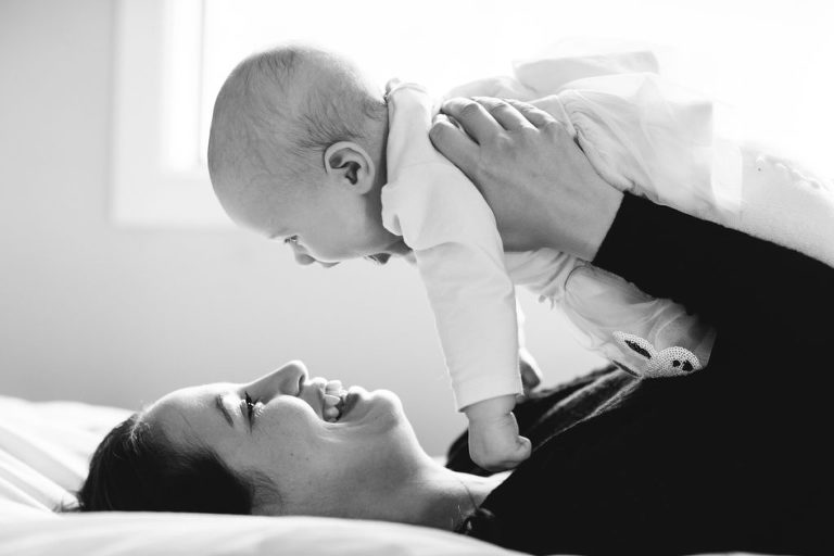 mum with baby in the air on bed natural light black and white Wellington family photography