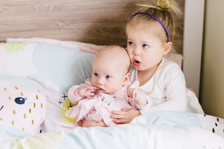 little girl and baby embracing on the bed staring off to the side natural light Wellington family photography