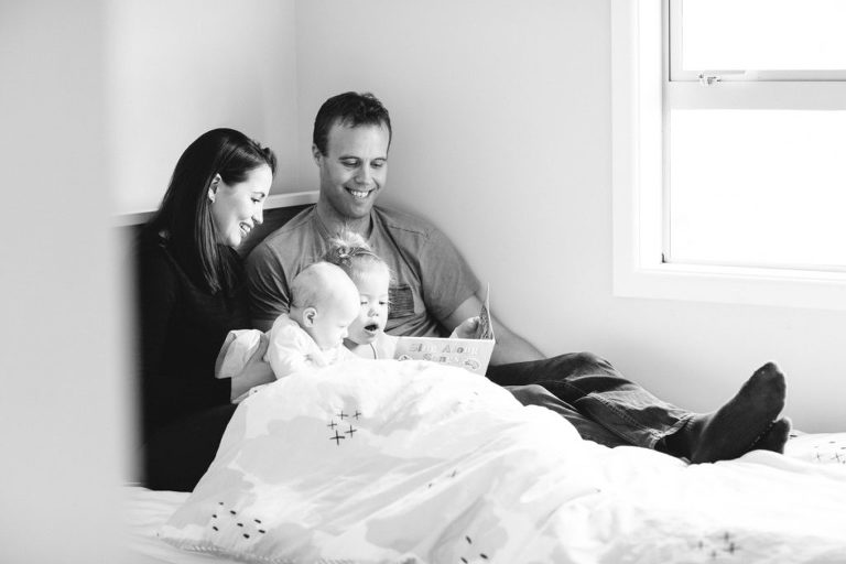 mum and dad on bed with sisters reading a book natural light black and white