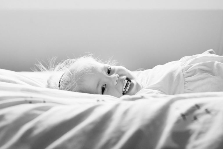 little girl smiling at camera on bed black and white natural light Wellington family photography